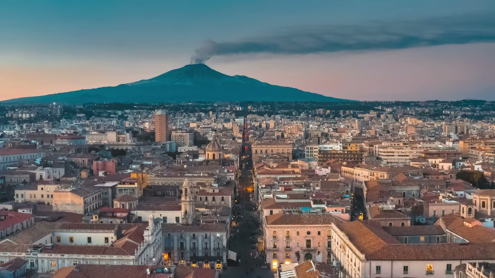 Catania dal drone al tramonto, con l’Etna che fuma sullo sfondo.